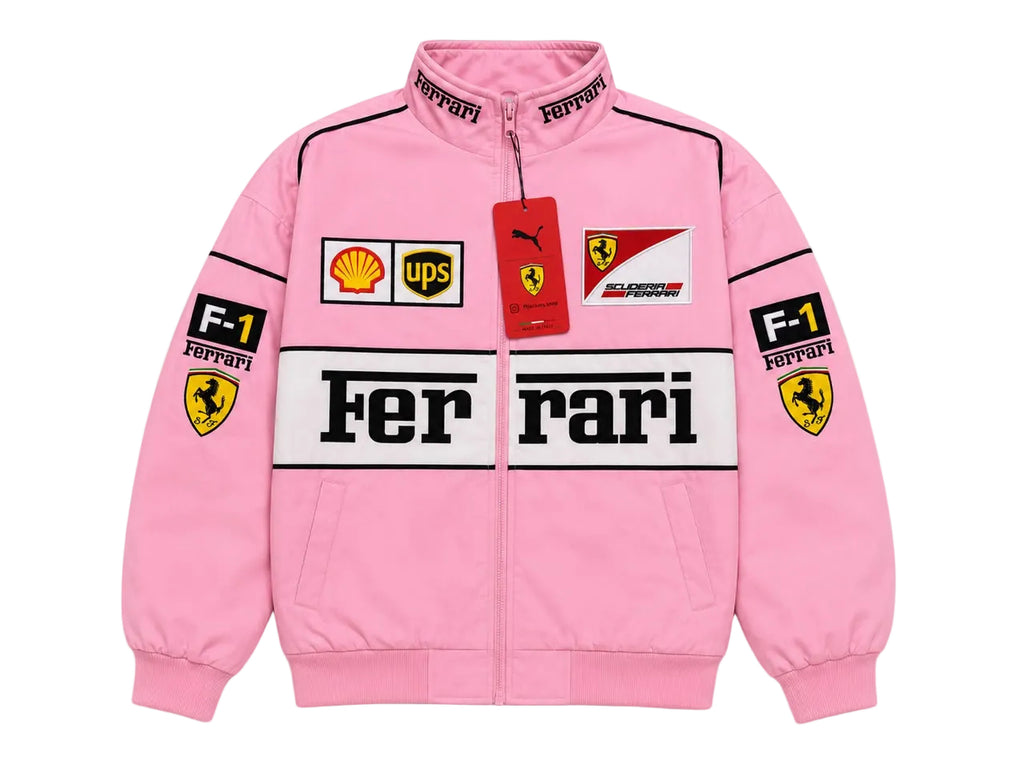 A pink Ferrari F1 racing track jacket with a full zipper, featuring the 'Ferrari' logo across the chest, 'Ferrari' and 'Puma' tags, and sponsor patches including Shell, UPS, and Castore on the front and sleeves.