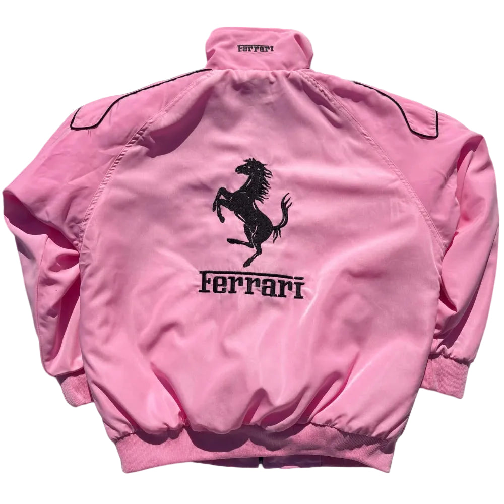 A pink satin windbreaker jacket shown from the back, featuring a black embroidered Ferrari prancing horse logo and the word 'Ferrari' on the center back, set against a solid black background.